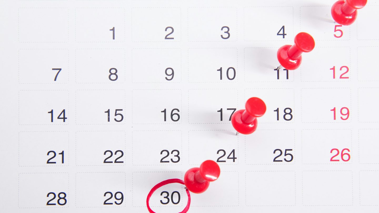 A monthly calendar with red push pins marking several dates