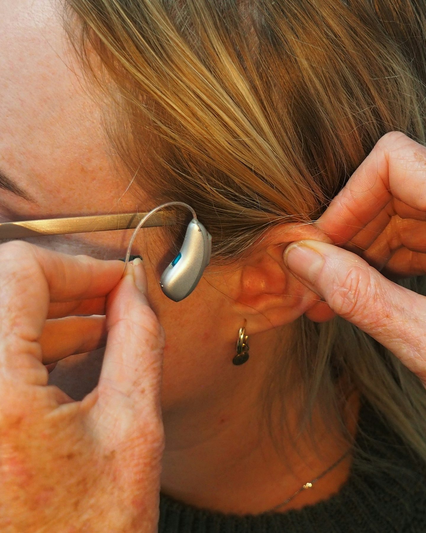 Hands fitting a behind-the-ear hearing aid on a woman