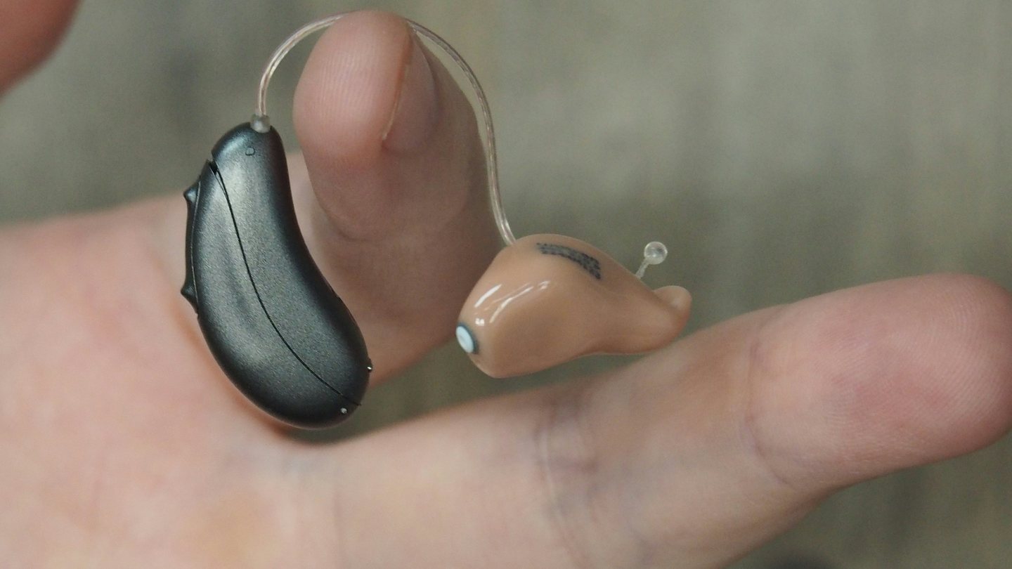 Two hearing aids resting on a hand