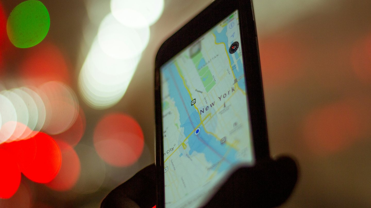 A phone showing a city map, held up against blurred city lights at night