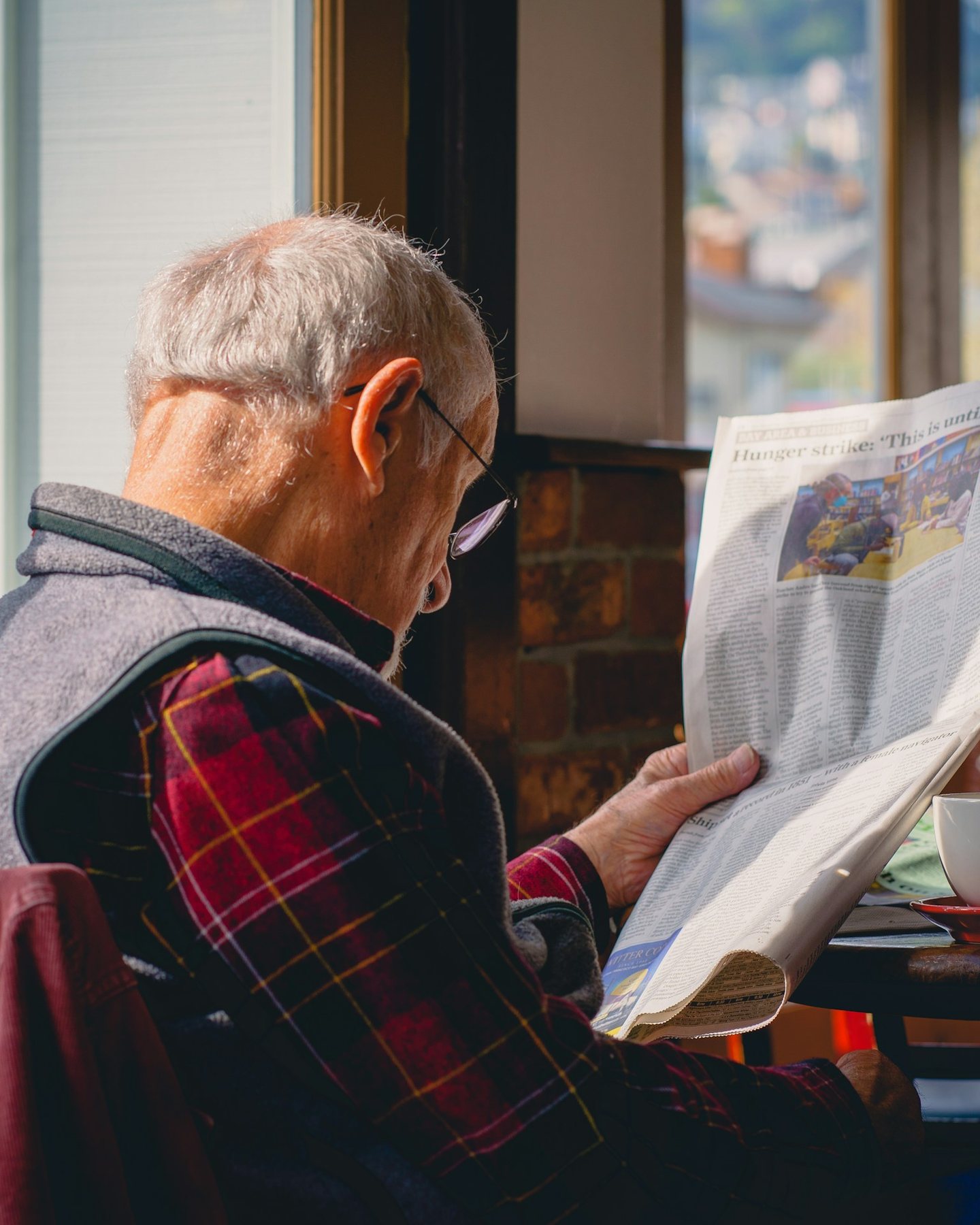 An older man reading the newspaper by a window