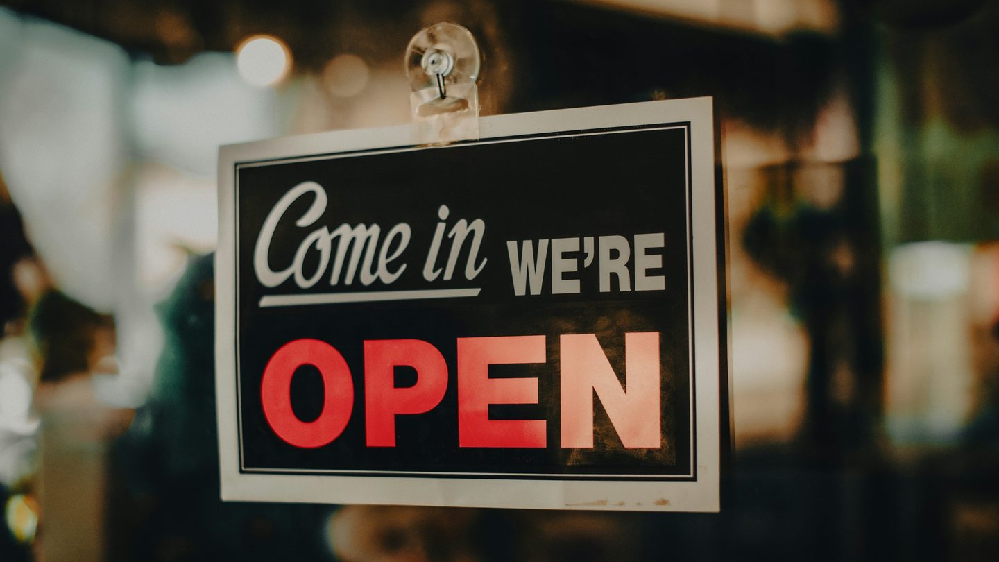 A “Come in, we're open” sign hanging in a shop's glass door