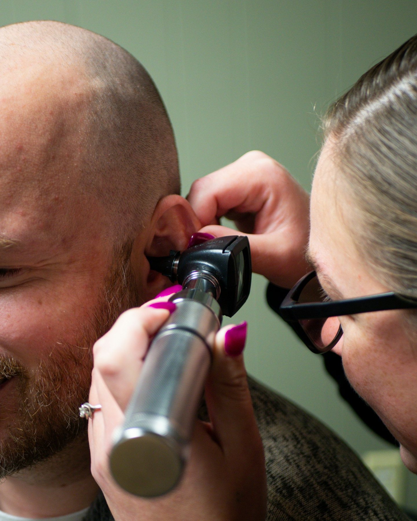 A clinician looking into a smiling patient's ear with an otoscope