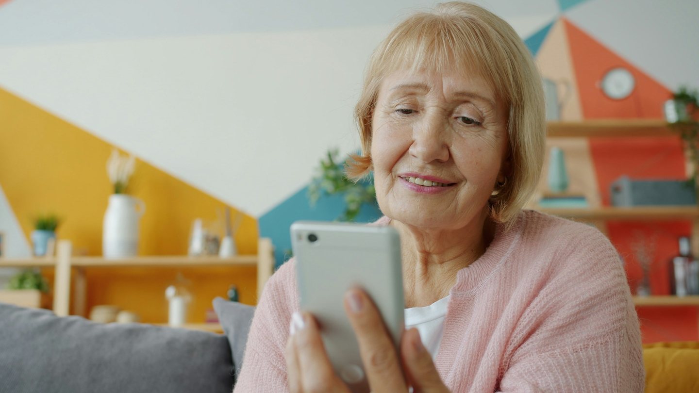 An older woman smiling as she reads on her phone