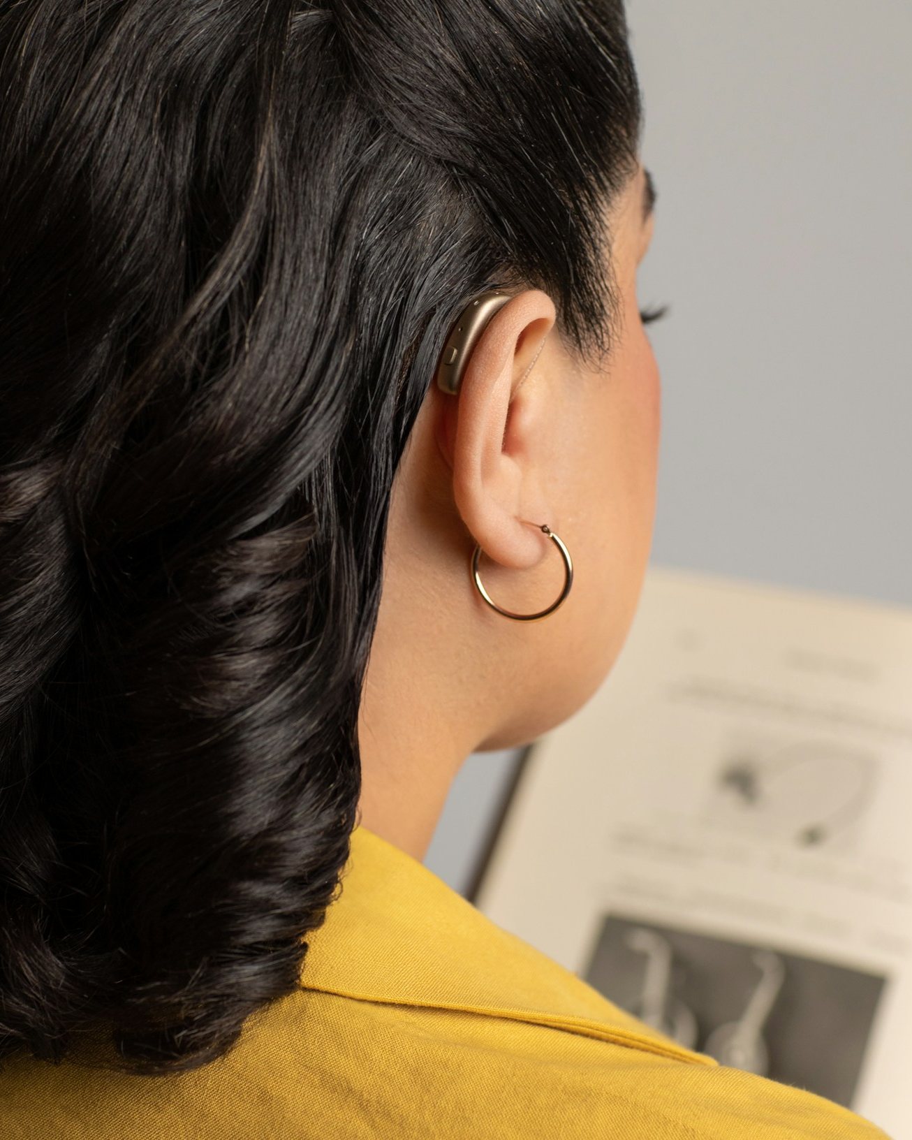 A woman wearing a hearing aid reads at home