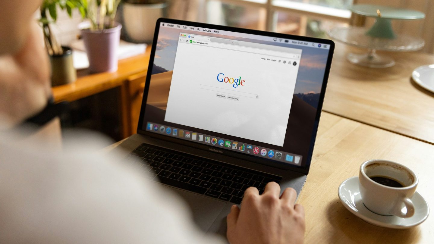 A laptop open on the Google search page beside a cup of coffee on a café table